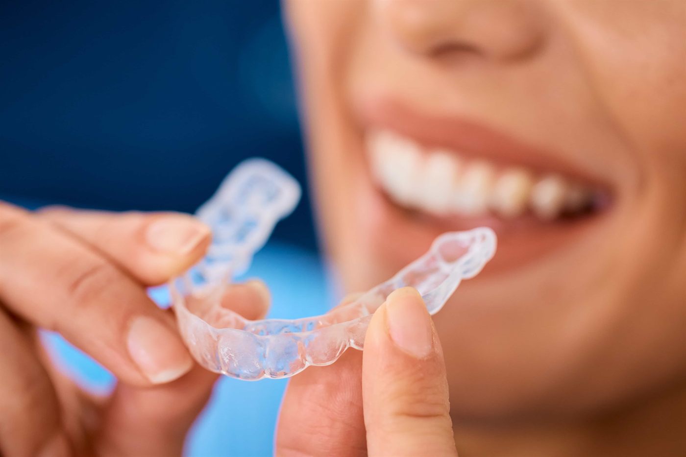 A smiling patient holding her clear Invisalign aligner